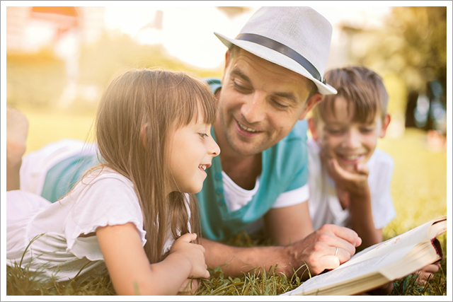 Father reading a book to his children outdoors